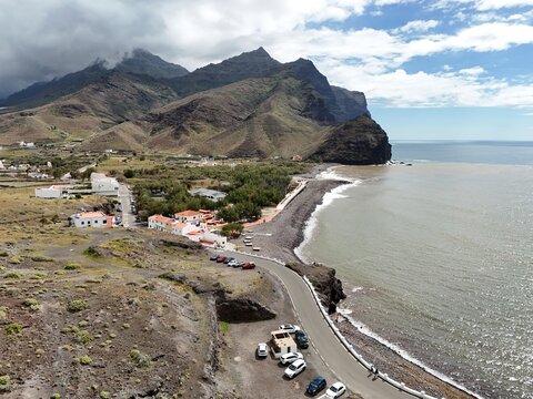 Aerial view of the dramatic coastline where the dark sand beach meets the turbulent sea under a sky heavy with clouds, Puerto de la Aldea, Canarias, Spain.