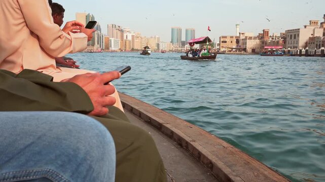 Dubai, UAE - 17th january, 2026: Traditional wooden abra crossing Dubai Creek. Tourist local passengers using smartphones with the historic Deira skyline and modern towers in the background