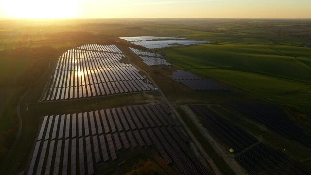 Aerial view of the extensive Tye Lane Solar farm with rows of panels reflecting the golden sunset light, contrasting with the green fields, Ipswich, United Kingdom.
