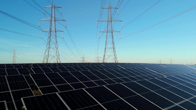 Aerial view of Tye Lane Solar farm, contrasted by the dark panels against the clear sky and towering electricity pylons, Ipswich, United Kingdom.