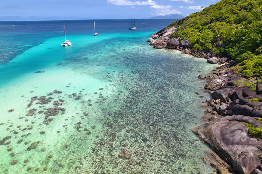  Drone of Mountain side, lush forest with granite rocks, docked catamaran and boat on low tide at cap ternay, Mahe, Seychelles