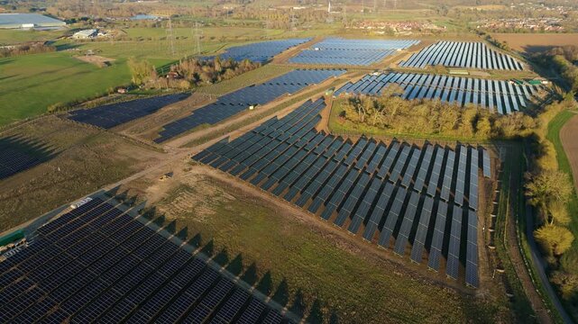 Aerial view of the extensive Tye Lane Solar farm, a sprawling grid of dark solar panels contrasting with the surrounding green fields, Ipswich, United Kingdom.