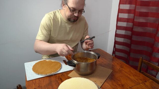 Man spreading wafer cakes with condensed milk. Simple cake. Sweet food at home. Hands spread cream with knife.