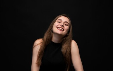 Fototapeta premium Happy young woman posing on a black background, expressing joy and laughter with a positive emotion and vibrant energy