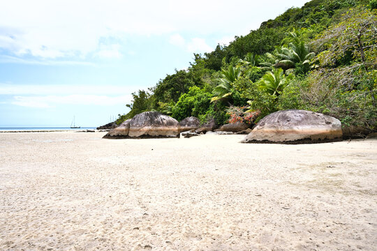 Low tide, granites stones, sunny day, white sandy beach, catamarans docked near the shore of cap ternay, Mahe, Seychelles