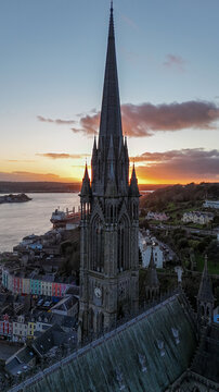 Aerial view of the majestic cathedral spire piercing the twilight sky, standing tall over the vibrant town and the tranquil waters, Cobh, County Cork, Ireland.