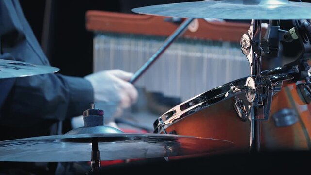 Dynamic close-up of a drum set on stage. Shiny cymbals in the foreground with a blurred musician playing a percussion instrument in the background