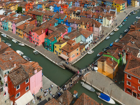 Aerial view of vibrant, multicolored houses lining narrow canals, a tapestry of vivid hues reflecting in the water, Burano, Veneto, Italy.