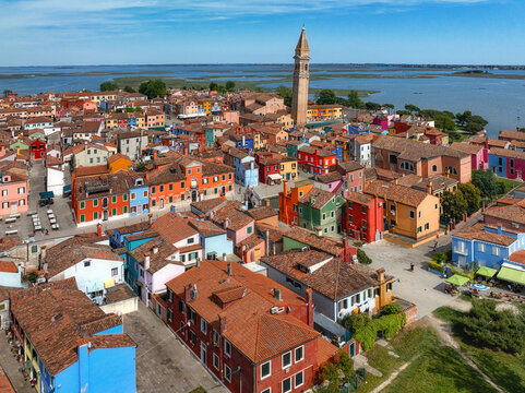 Aerial view of a vibrant tapestry of multicolored houses with terracotta roofs clustered tightly together, punctuated by the soaring campanile of Burano, Venice, Veneto, Italy.