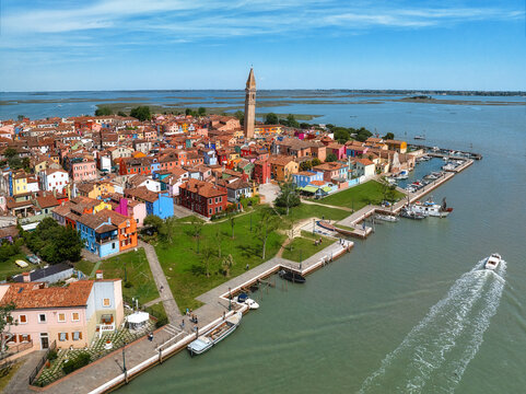 Aerial view of the vibrant Burano island, a kaleidoscope of colorful houses under a clear sky, with the iconic leaning bell tower of San Martino, Venice, Veneto, Italy.