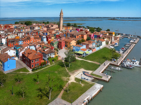 Aerial view of vibrantly colored houses clustered around the leaning bell tower of Burano, a picturesque island with a bustling marina and serene waterways, Venice, Veneto, Italy.
