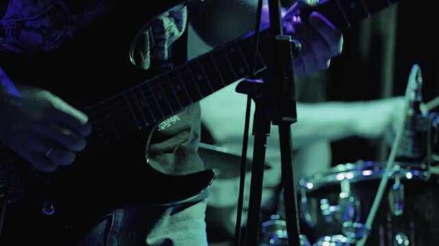 Close up of a guitarist's hands playing an electric guitar during a live performance. Dramatic red stage lighting create an energetic, intense mood for a rock metal concert