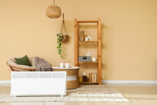 Interior of stylish living room with modern electric convector heater, coffee table and armchair