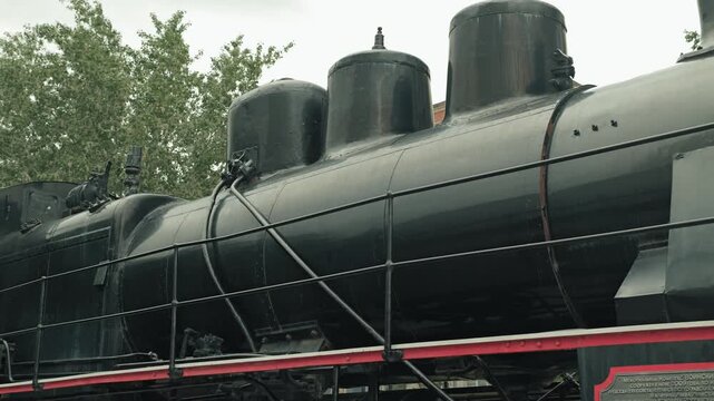 Side view of a vintage black steam locomotive. The powerful machine showcases elements of industrial design boiler, pipes, and railings. Muted tones and overcast lighting create a nostalgic atmosphere