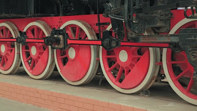 Detailed side view of a historic steam train's undercarriage. Bright red wheels contrast with the black industrial machinery. A nostalgic, powerful image perfect for transportation or history themes
