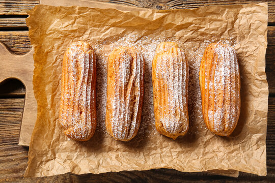Board with tasty eclairs on wooden background