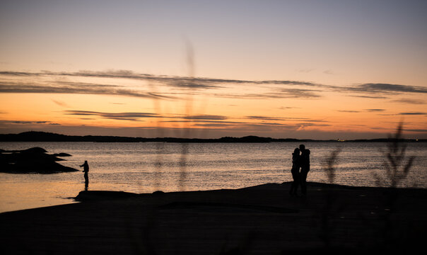 Silhouetted couple kissing by the sea at dusk.