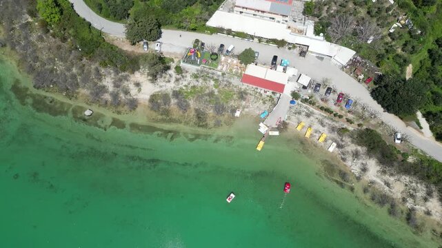 Aerial drone video of Lake Kournas in Crete. The footage shows colorful pedal boats gliding on turquoise freshwater, a scenic shoreline, and tourist infrastructure. High quality 4k footage