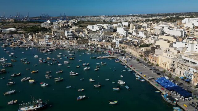 drone view of colorful luzzu boats in Marsaxlokk bay, Malta, calm water and fishing village
