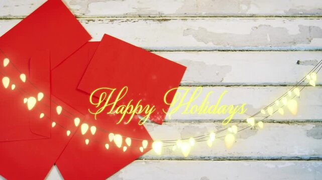 Animation of happy holidays text over red envelopes on wooden background