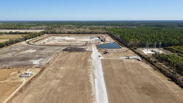 Aerial view of construction site with contrasting textures of bare earth and lush greenery, reflecting the clear blue sky, Elkton, Florida, United States.