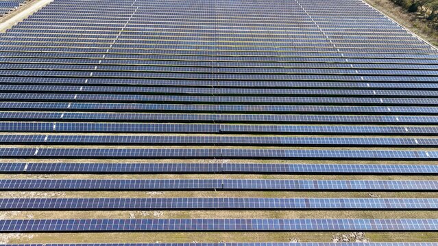 Aerial view of a vast solar panel array stretching into the horizon, reflecting the sky in stark contrast to the dry earth, Elkton, Florida, United States.