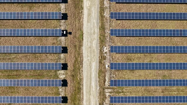 Aerial view of neatly arranged solar panels casting shadows on the arid land alongside a sandy path, Elkton, Florida, United States.