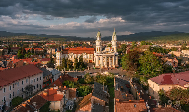 Aerial view of a grand cathedral with twin spires, its white facade gleaming amidst the rustic rooftops under a dramatic sky, Uzhhorod, Zakarpattia Oblast, Ukraine.