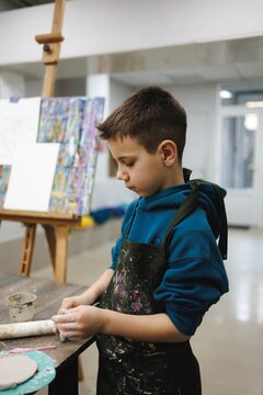 Young boy focused on shaping clay in art studio with paint splatters around him