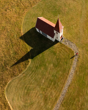 Aerial view of the stark white church with its red roof stands out in the Icelandic landscape, casting a long shadow, Hellnar, Snaefellsbaer, Iceland.