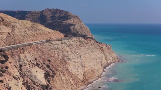 Aerial drone view of a winding coastal road running along steep white cliffs above the turquoise Mediterranean Sea in Cyprus