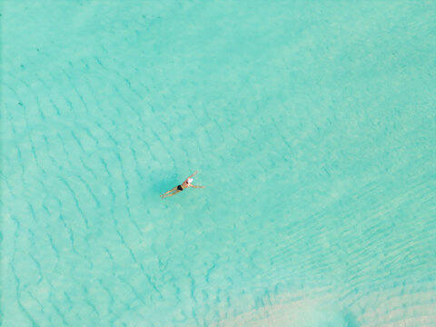 Aerial view of a swimmer in the turquoise waters, a serene escape in the pristine seascape of Kan island, Dhidhdhoo, Thiladhunmathi Atoll, Maldives.