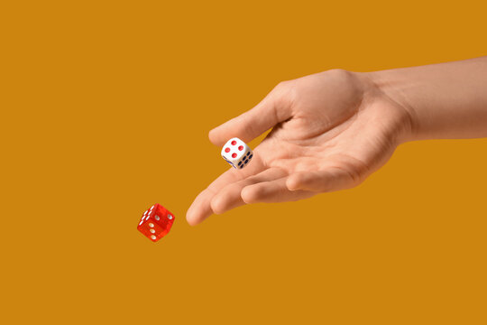 Female hand throwing game dices on orange background