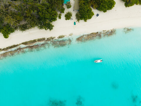 Aerial view of a lone boat cuts through the turquoise waters, framed by the white sandy beach and the lush green vegetation of the island, Vashafaru Island, Thiladhummathi Atoll, Maldives.