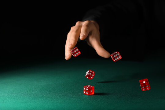 Male hand throwing red game dices on green table against black background