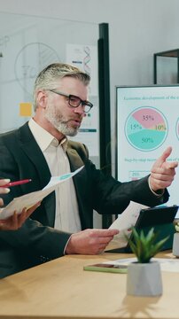Good-looking successful experienced responsible heads of departments sitting arounf workdesk in modern boardroom and discussing indicators of economic development of their enterprise in recent years