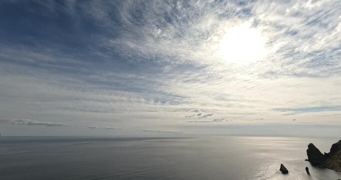 Seascape sky clouds vast ocean horizon under dramatic cirrocumulus clouds and bright sun over rugged coastal rocks