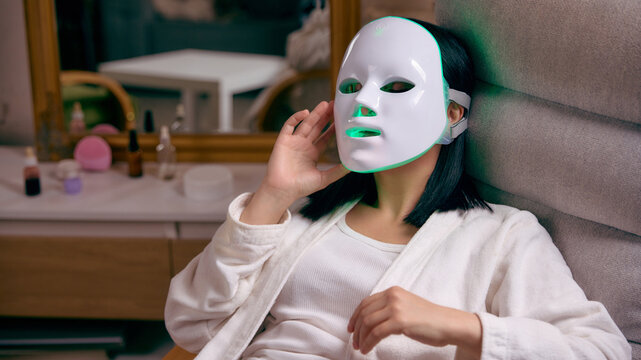 Woman wearing led facial mask for skincare treatment at home. Concept of beauty technology, anti aging therapy, cosmetic device usage, skin rejuvenation routine, modern self care.