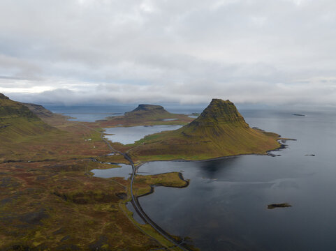 Aerial view of Kirkjufell mountain rising majestically from the sea, its green slopes contrasting with the dark waters, Grundarfjordur, Iceland.