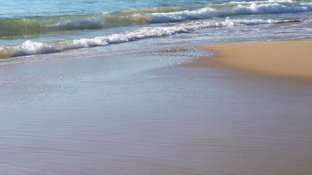 Close view of ocean waves washing over sand with sea foam, Tathra, New South Wales, Australia.