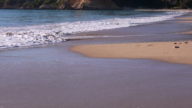 Ocean waves rolling onto sandy beach with gentle surf, Tathra, New South Wales, Australia.
