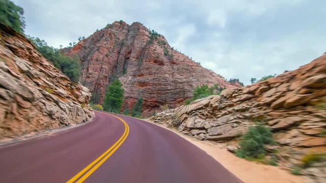 Experience the stunning, breathtaking beauty of Zion National Park from the perspective of a scenic drive. The footage captures the winding road as it passes between towering, sheer cliffs of red and 