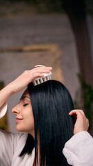 Woman massaging scalp with brush during hair care routine. Concept of hair treatment process,...