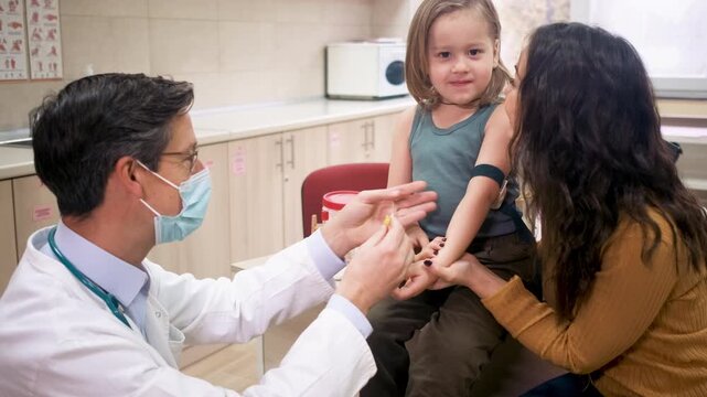 Mother comforting young child before blood test at pediatric clinic with male doctor.