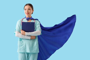 Female Asian doctor with superhero cape and clipboard on blue background. International Nurses Day © Pixel-Shot