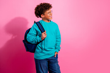 Smiling schoolboy with backpack looking to the side against a pink background, casual student portrait in turquoise sweater and jeans © deagreez