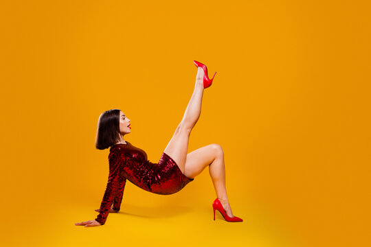 Woman in red sequin dress and high heels striking a playful fashion pose on a bright yellow studio background
