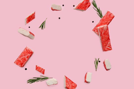 Frame made of cut tasty crab sticks with peppercorns and rosemary flying on pink background