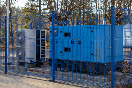 Blue industrial power generator and air conditioning unit securely fenced outdoors, representing essential energy infrastructure and reliable utility services