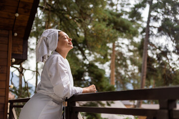 Fototapeta premium a woman in a white robe and a towel on her head, with mountains in the background, in a hotel